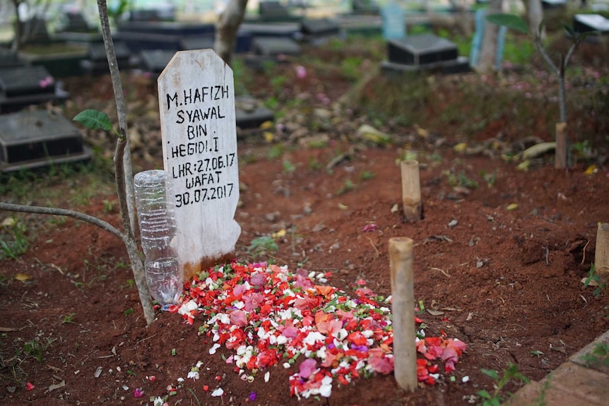 A temporary headstone sits at the head of a tiny grave covered in flowers