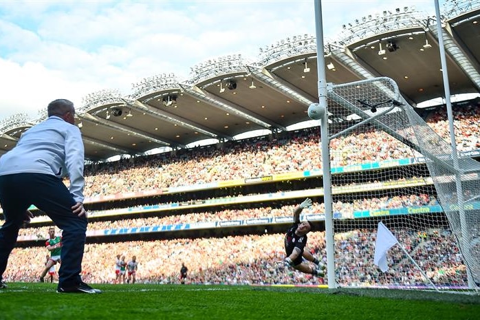 An official watches as a Gaelic football goalkeeper dives as the ball hits the post and goes wide in the All-Ireland final.