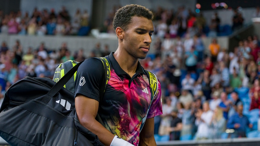 Felix Auger-Aliassime carries his tennis bag off the court after losing at the Australian Open.