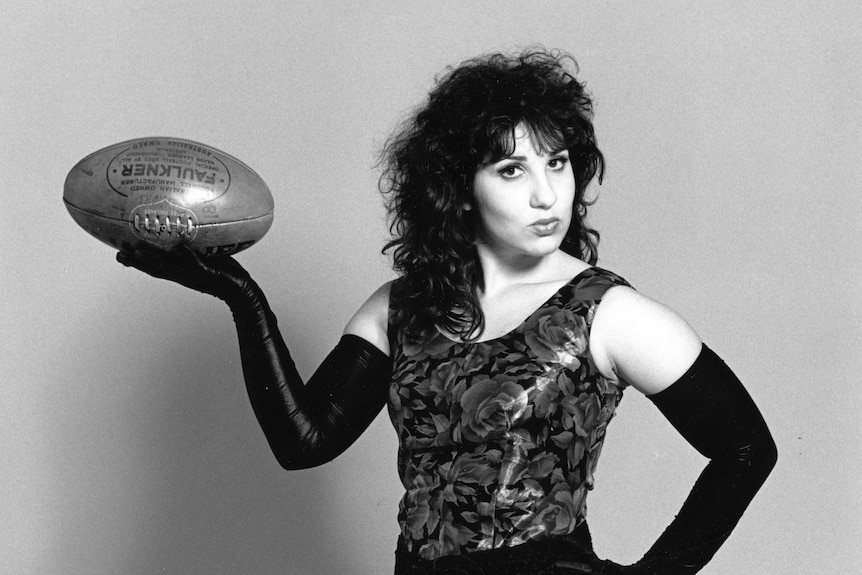 Black and white photo of Libbi Gorr in a dress holding a football, sassy look on face.