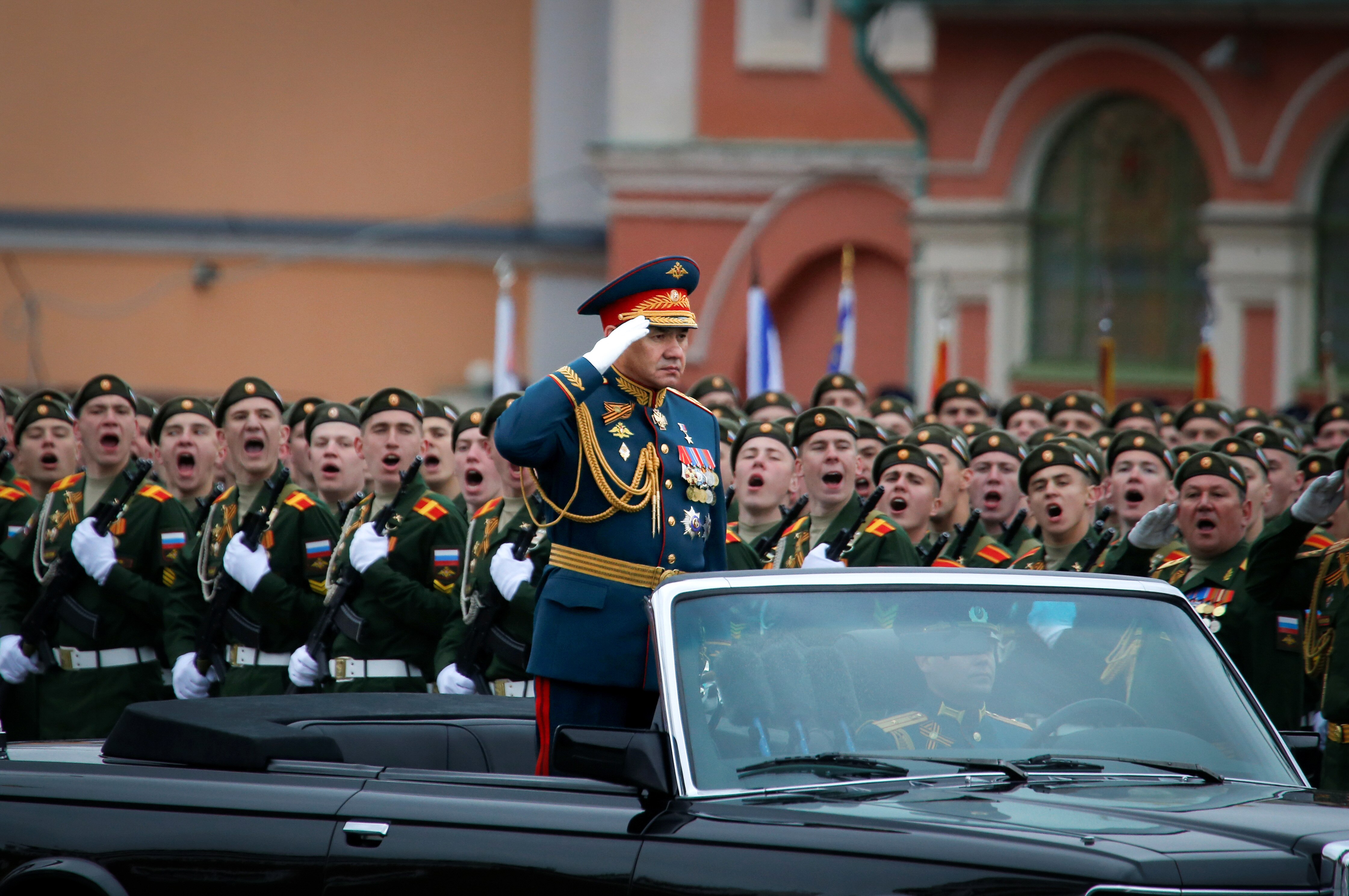 Sergei Shoigu saluting while standing in an open top car