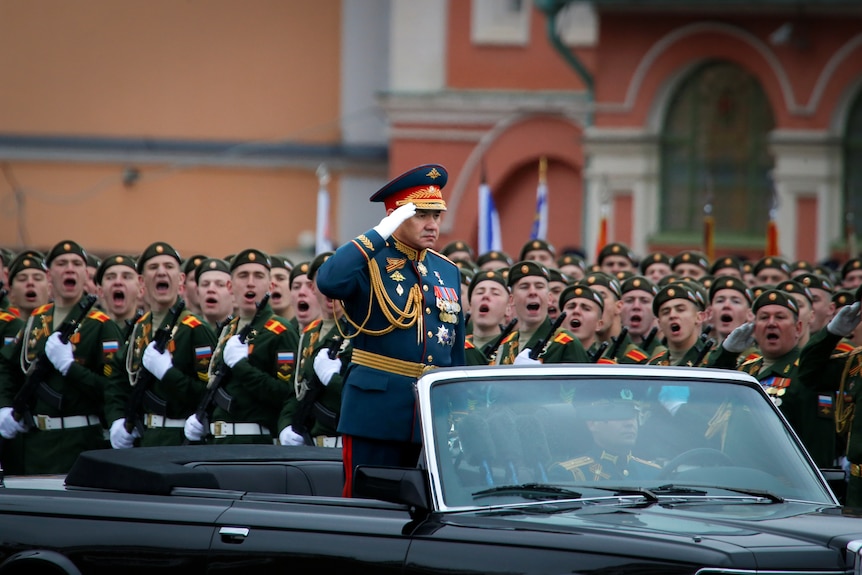 Sergei Shoigu saluting while standing in an open top car