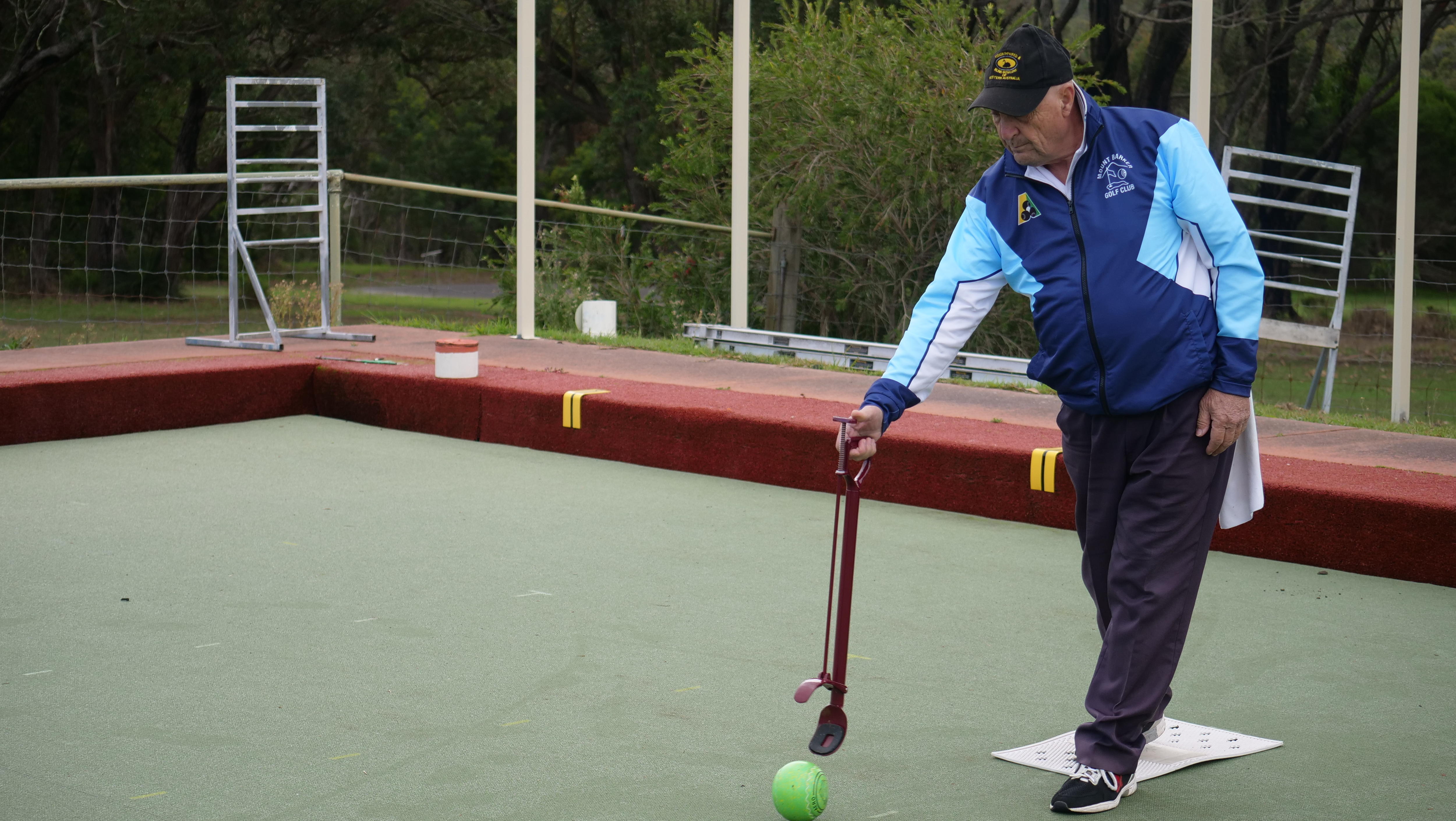 A middle-aged man on a bowling green has a roll using a clamp.