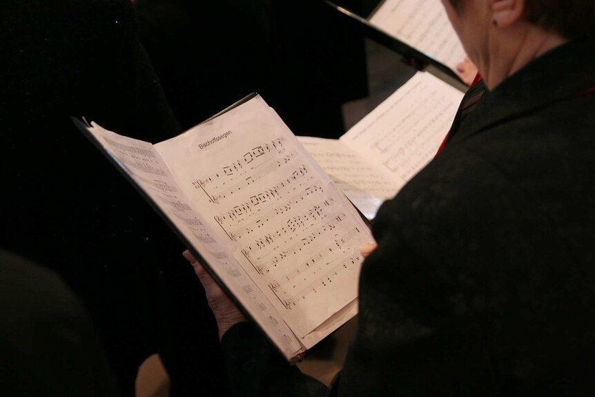 A woman reads from sheet music in a choir.