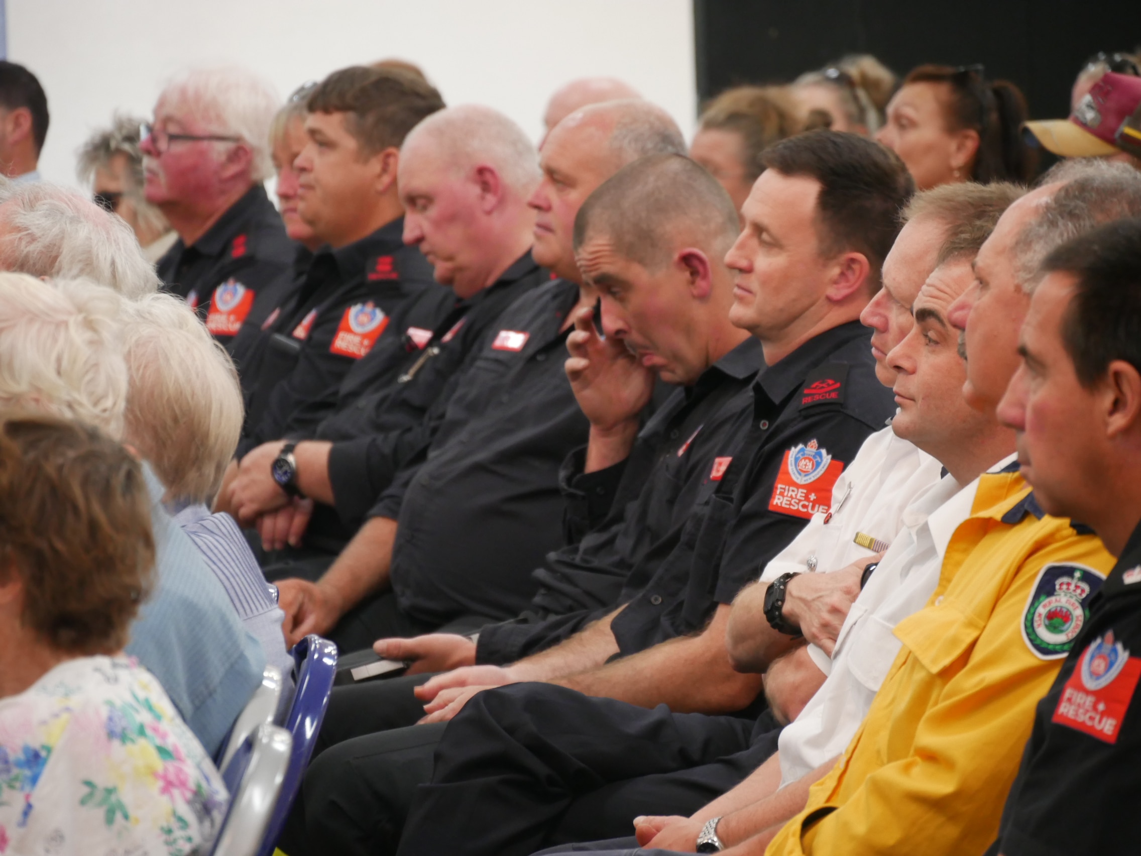 Fire and Rescue personnel sit in a crowd, one wiping his eyes.