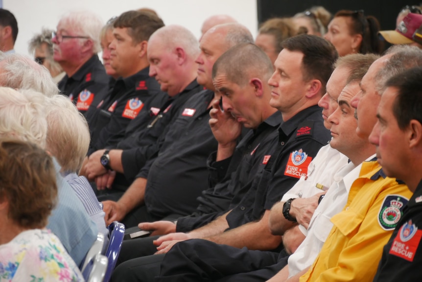 Fire and Rescue personnel sit in a crowd, one wiping his eyes.