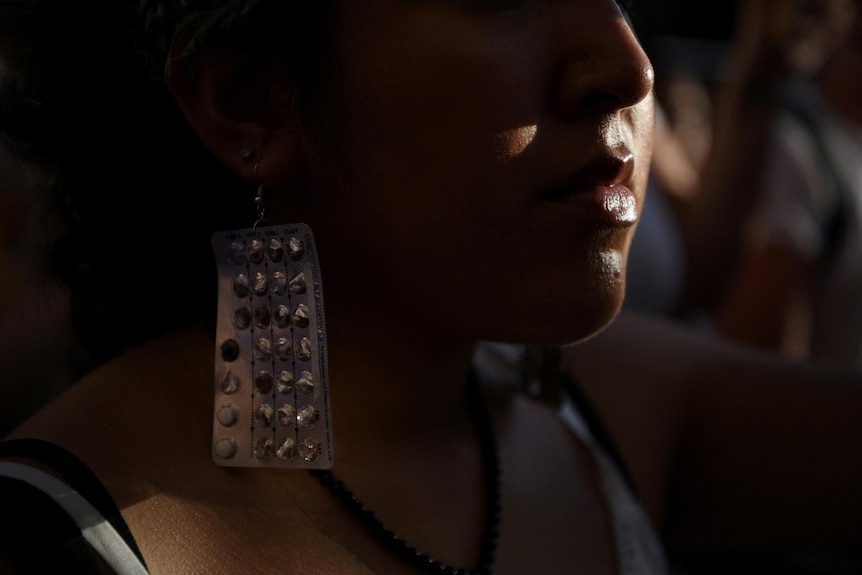 A woman wears a pair of birth control pill packets as earrings