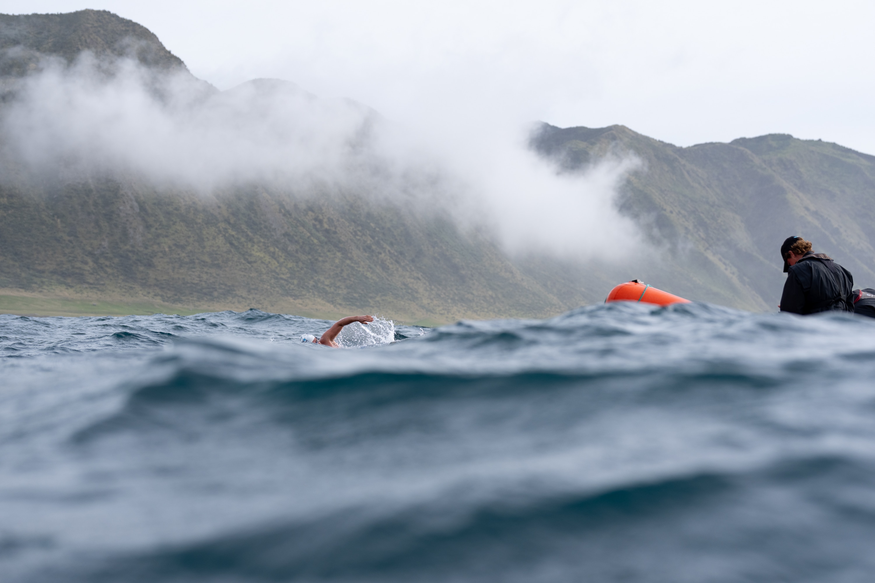 Jono Ridler swims next to a mountainous coastline