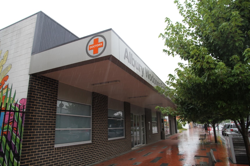 Outside the brick building labeled Olbury Wo Donga Family Medical Center. 