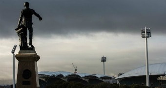 A statue of a man pointing his finger ahead overlooks an arena as skies of grey take over Adelaide.