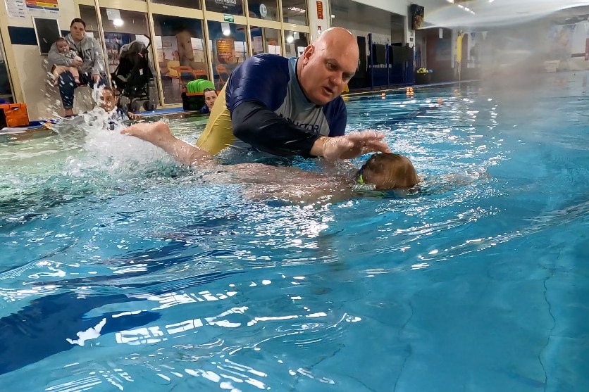 A man in a pool with a child swimming. 