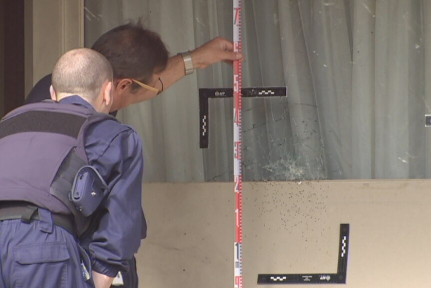 Police inspect bullet holes in front window and wall of a south Canberra home.