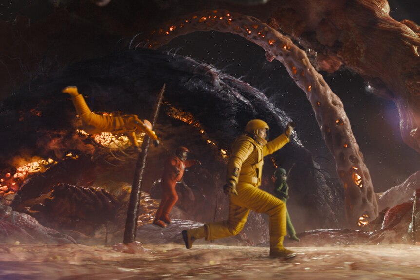 Three characters from Guardians of the Galaxy, one in a yellow space suit, in a fiery action sequence from the film.
