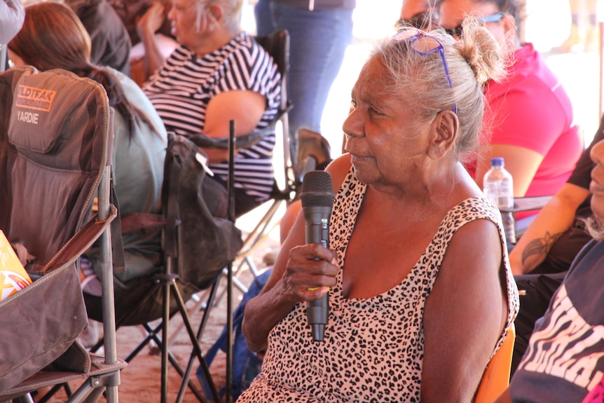 a women sitting on a camp chair holding a mic.