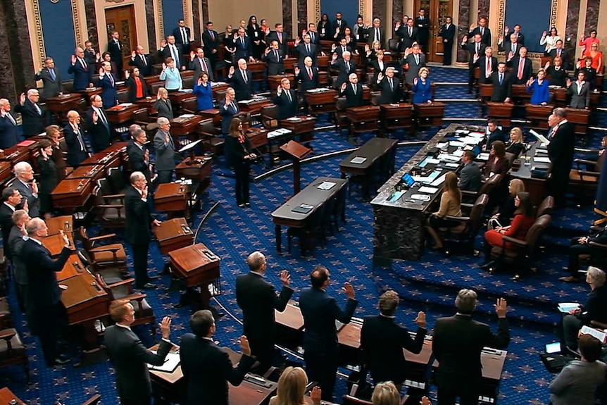 US Senators stand with with right hands raised, taking the oath of impartiality ahead of Trump's impeachment trial
