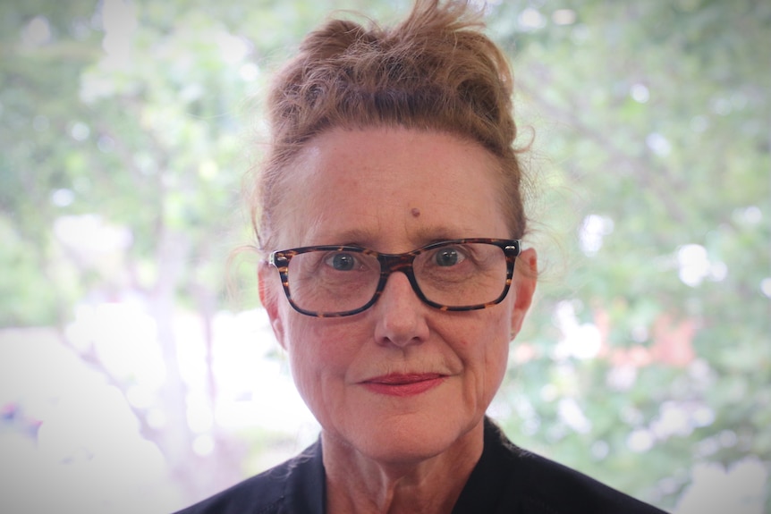 A woman with glasses and tied up red hair poses for a close up photo