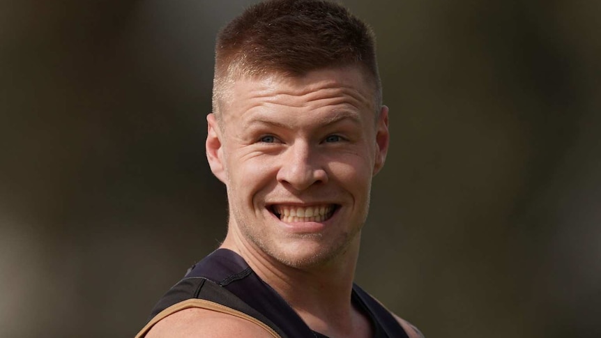 Collingwood footballer Jordan De Goey, wearing a dark singlet, is pictured smiling.