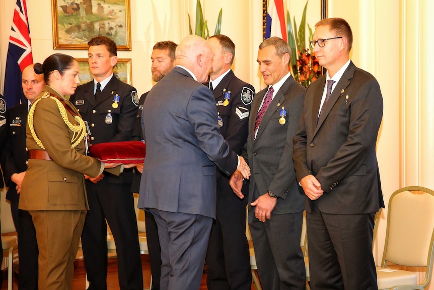 Governor-General Peter Cosgrove shakes hands with one rescuer as others stand in a line beside him.