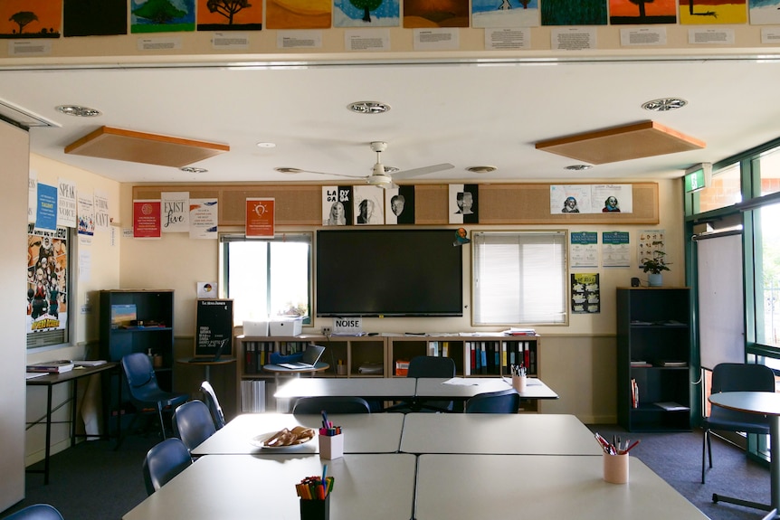 Classroom with desks in foreground and large screen tv in the background.