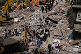 Rescue workers carry the body of a victim on a stretcher and cranes looking for other victims under the rubble.