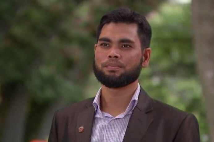 A Rohingya man with a short beard standing in a blazer and looking into the middle distance.