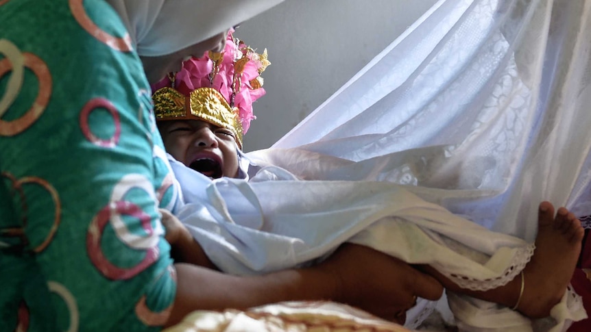 A baby being held down and surrounded by sheets before she undergoes circumcision.