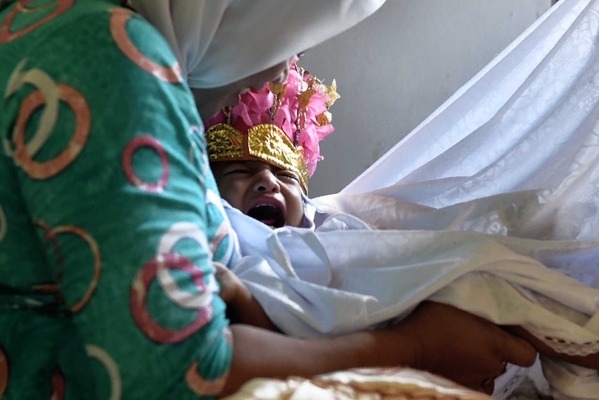 A baby being held down and surrounded by sheets before she undergoes circumcision.