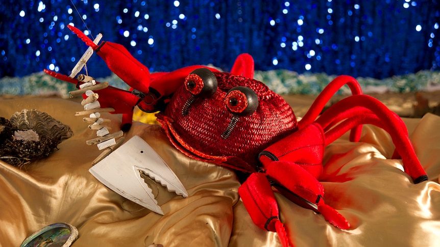 A bright red, handmade crab puppet smiles up from a gold pillow.