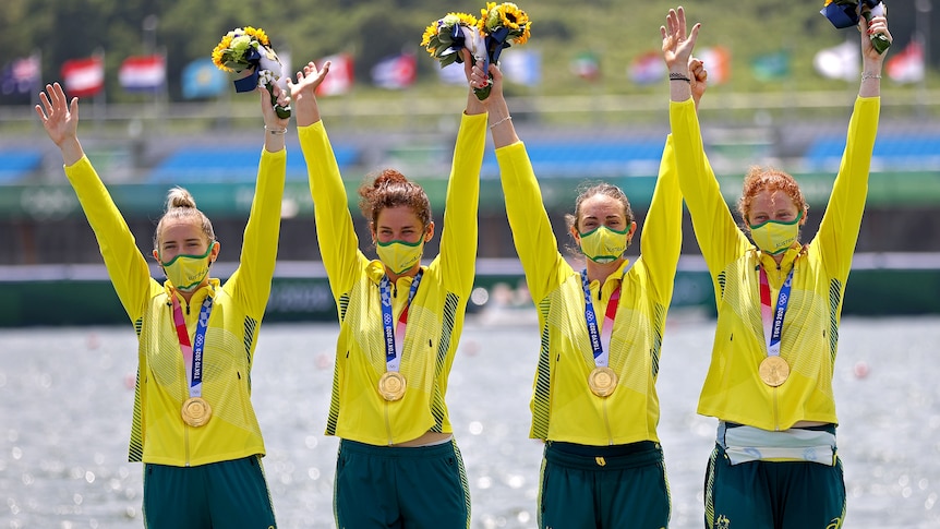 Four women wearing yellow jackets hold their arms in the air