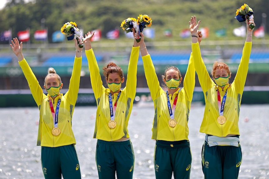 Four women wearing yellow jackets hold their arms in the air