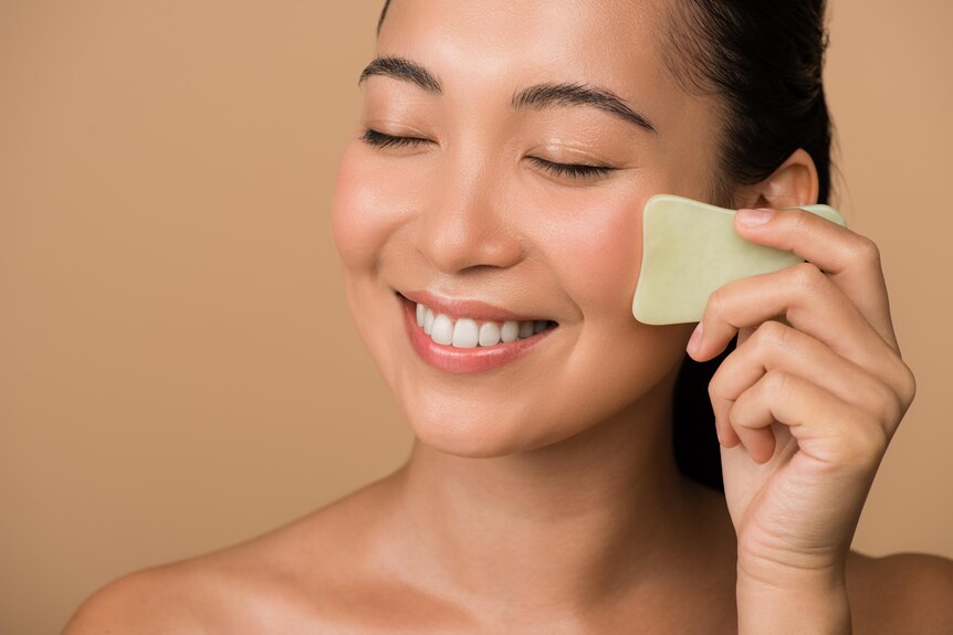 asian woman doing gua sha on her face with a tool