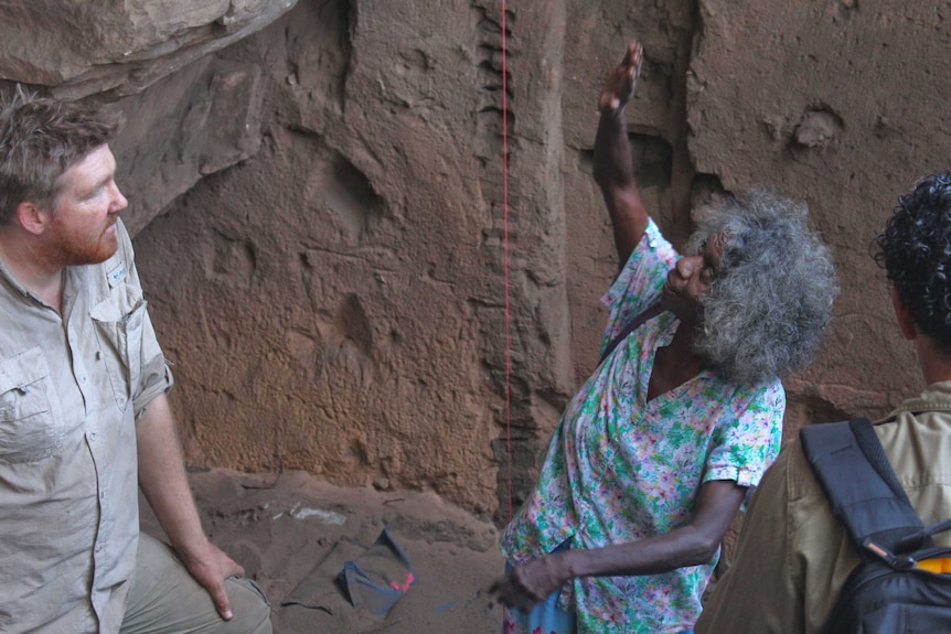 An Aboriginal woman gestures upwards while a man watches her. Both are in an excavation pit.