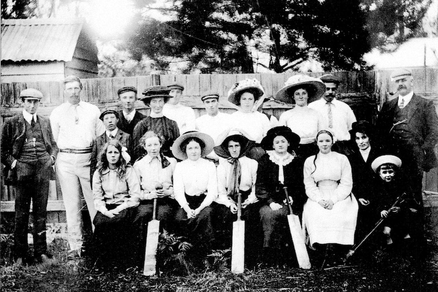 Black and white group photo of a women's cricket team, some of the women are holding bats and everyone is wearing a hat