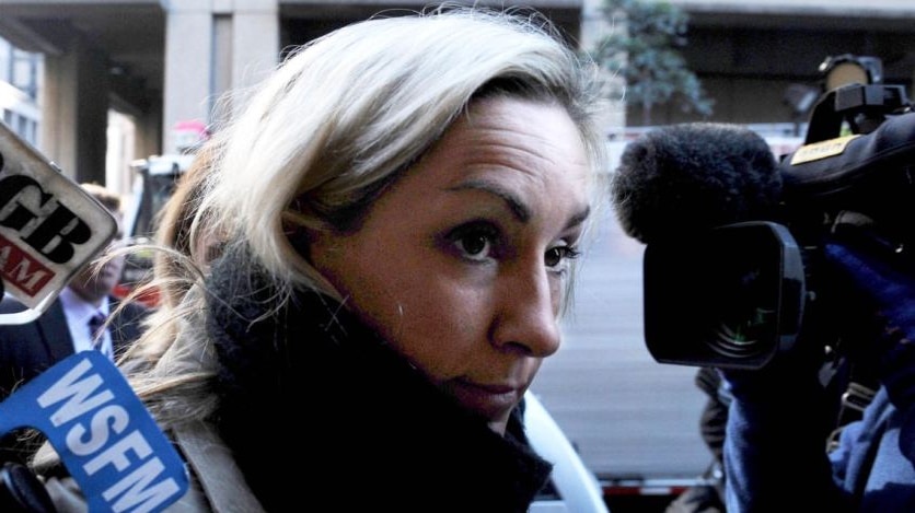 Woman wearing scarf surrounded by media microphones