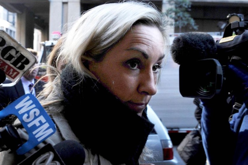 Woman wearing scarf surrounded by media microphones