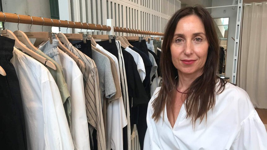 Bassike co-founder Deborah Sams stands beside a rack of clothes in a room.