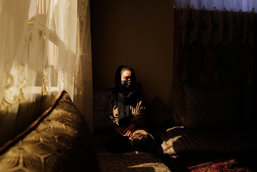 Woman sits in her home as the sun peaks through the window.