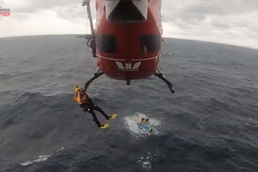 A rescuer hangs off the end of a helicopter.