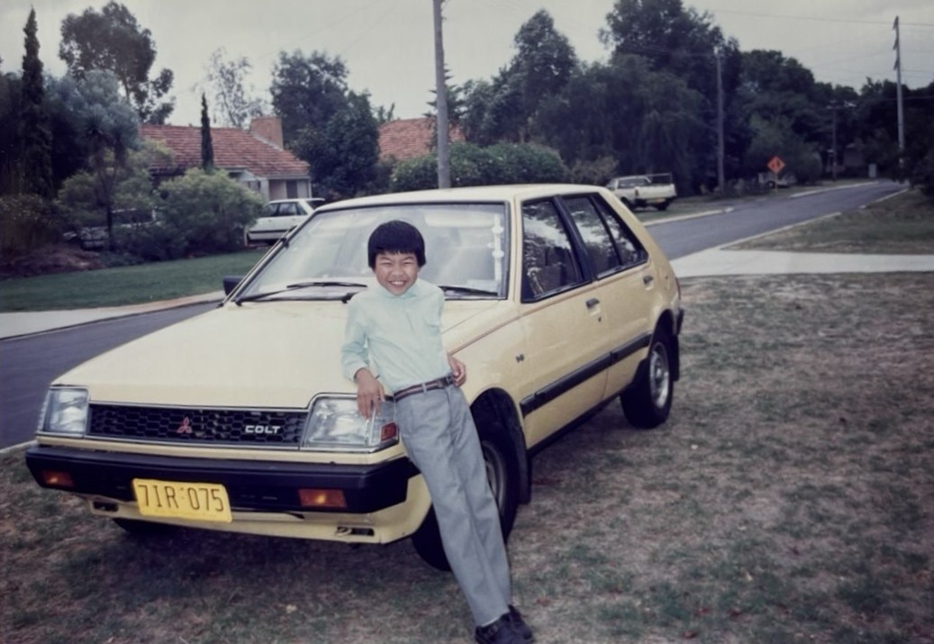 Um jovem de Hong Kong está encostado no capô de um sedã Ford amarelo no jardim da frente de uma casa. imagem retrô