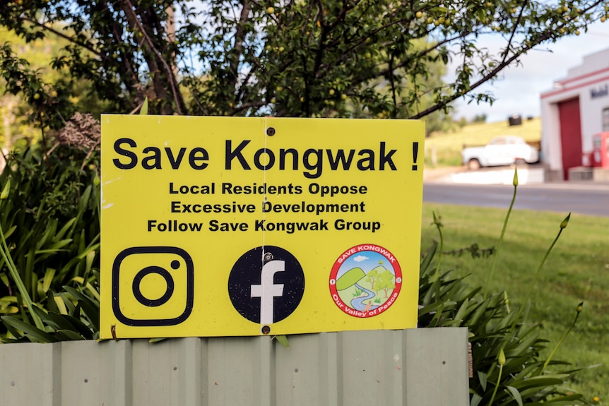 A  yellow sign on a fence next to a road reading Save Kongwak with logos for facebook and instagram