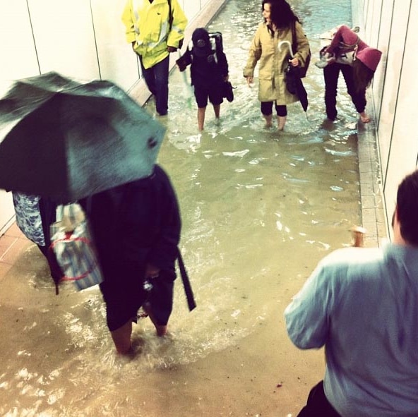 Commuters at Lewisham station in flooded pedestrian underpass.