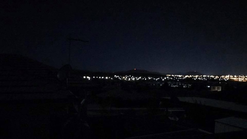 Darkness in the foreground with lights from a suburb in the background.