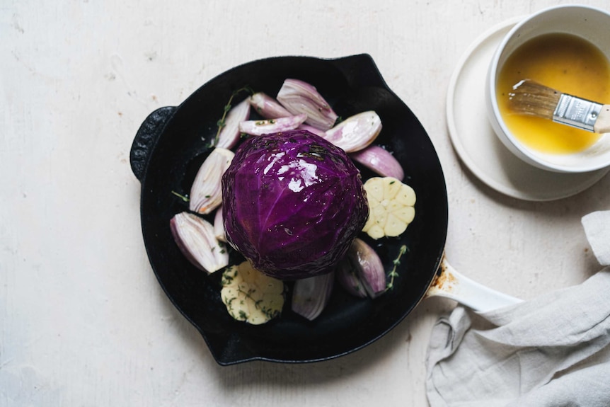A whole head of red cabbage sits on top of chopped shallots, garlic, brushed with a maple glaze, a vegetarian roast.