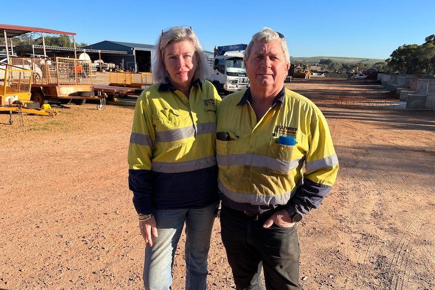 husband and wife Greg and Jo Stephen stand together in hi-vis at a timber yard. 