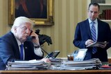 Donald Trump sits at desk talking on phone, Reince Priebus stands in the background. January 28, 2017.