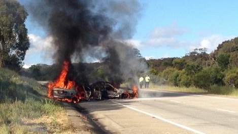 Police stand near the fiery wrecks of two cars on the Hume Highway.