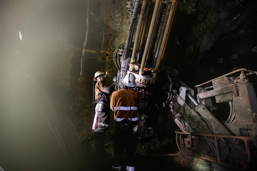 Two workers operate a large drill in an underground mine.