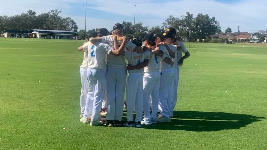 A group of junior cricketers form a huddle on an oval.