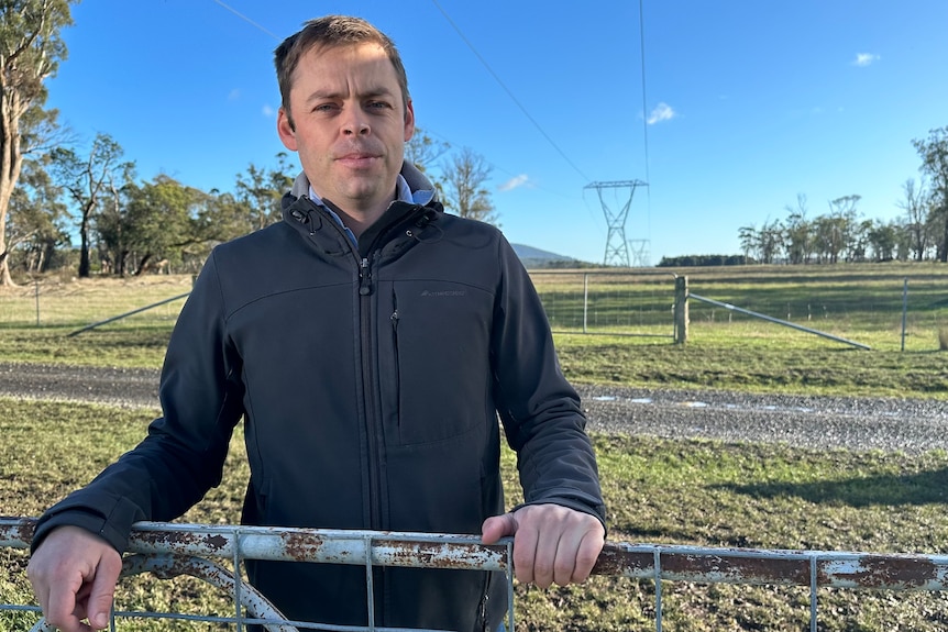 Farmer standing on his property in front of a transmission line. 