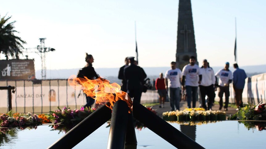 The Kings Park flame of remembrance burns in daylight with people in the background.